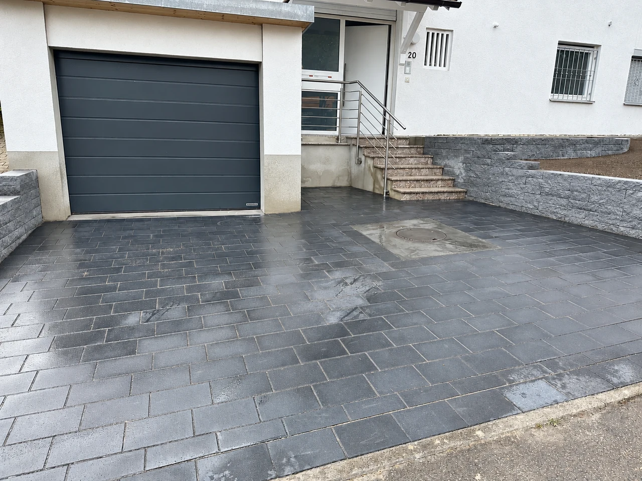 Gepflasterte Einfahrt mit Treppe und grauer Gartenmauer