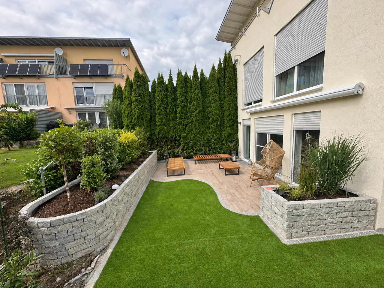 Terrasse mit geschwungenen Natursteinmauern, Beeten und grüner Rasenfläche