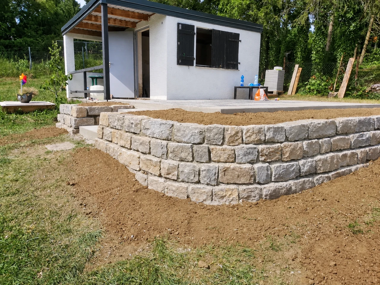 Helle Natursteinmauer vor einem Gartenhaus